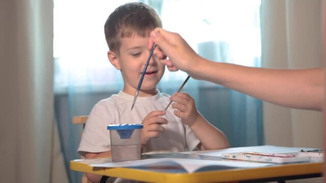 A boy draws with paints at a table in his room. High quality FullHD footageA boy draws with paints at a table in his room.