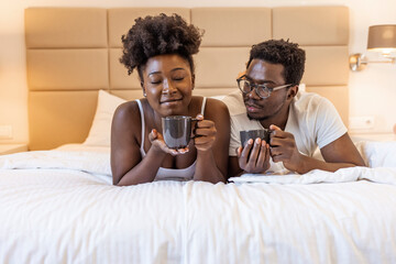 Shot of a happy young couple having coffee together in bed at home. Happy young couple talking and laughing while sitting on the bed and drink coffe in the morning at home.