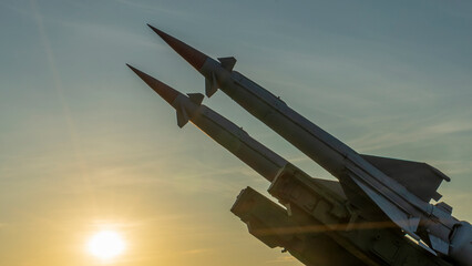 Two combat missiles aimed at the sky. Old ballistic missile launcher on blue sky background. - obrazy, fototapety, plakaty