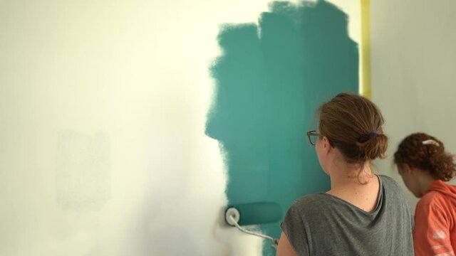 Mother and daughter painting wall in apartment room. Happy family doing repairs in new flat. Funny woman and teen girl making decorate room