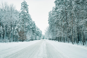 Winter forest with snowy road. Cars move on slippery road, dangerous driving