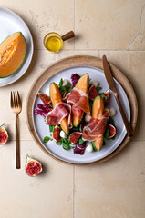 Fresh cantaloupe melon salad with prosciutto, figs, green leaves mix and mozzarella cheese. Top view, overhead, flat lay