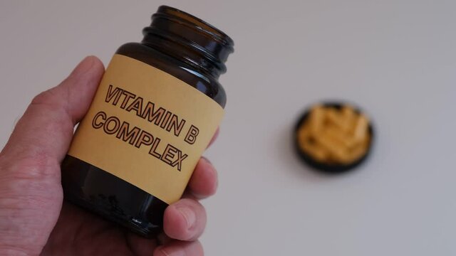 A man holding a bottle of Vitamin B Complex in his hand. Close up.