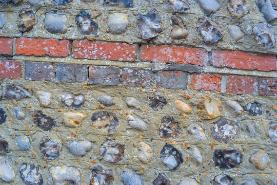 A stone wall that is common in England. A wall of large stones hidden with cement small round gray stones, turn a double row of red bricks