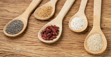 Assorted superfoods in spoons over wooden table. Chia, quinoa, oat, linseed and goji berry