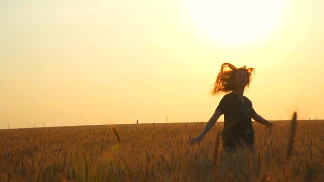 A woman runs across the field at sunset. free spirit of a beautiful young girl. Collect rye and wheat. Enjoy the summer and be happy. Spin and laugh. Warm sunny day in summer. Evening in the village.