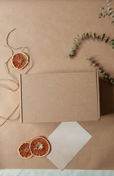 Overhead view of a package ready to wrap in brown paper with a blank envelope and rustic eucalyptus and orange decorations
