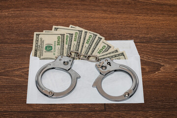 Envelope with dollars on a wooden background. Steel handcuffs on the envelope. The concept of...