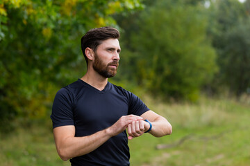 Fototapeta premium Sport Caucasian man looking smart watch at modern track runner using use smartwatch fitness bracelet Portrait fit male athlete checking result jogging in sportswear in street urban city park outdoor