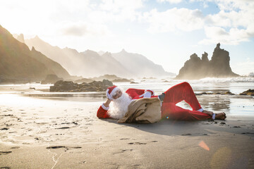 Obraz premium Funny conceptual photo of Santa Claus lying and relaxing on tropical beach at the ocean.
