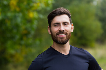 Close up portrait young happy bearded man standing in nature between forest trees relaxes, breathes fresh air closing his eyes. Male enjoys a life of peace calm, quiet in the park. Outdoors. Happiness