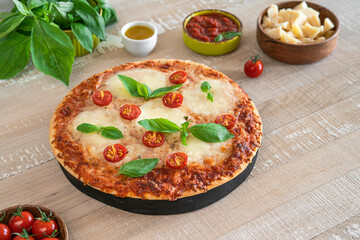 Background with margarita pizza on light wooden table. Traditional italian food: delicious pizza with mozzarella and cherry tomatoes
