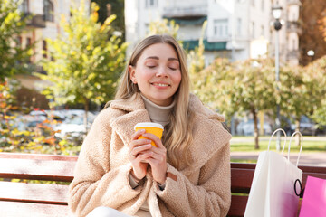 Beautiful happy woman smiling with her eyes closed, enjoying coffee in the park on warm sunny autumn day