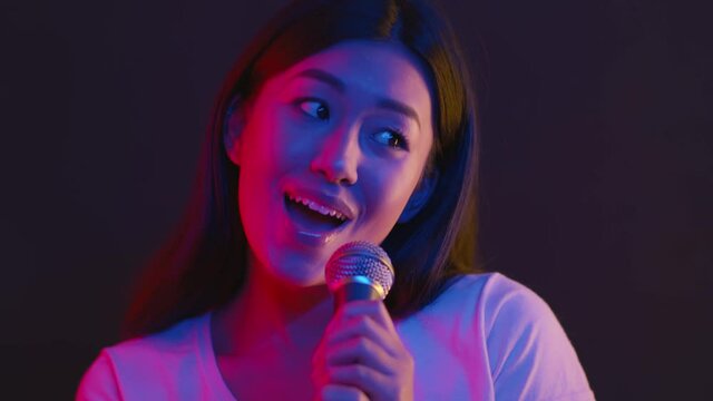 Nightlife entertainment. Young asian woman singing into microphone at karaoke, dancing on stage in bright neon lights