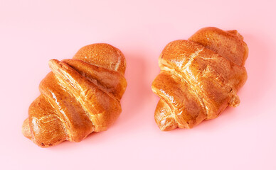 Two French croissants close-up on a pink background.