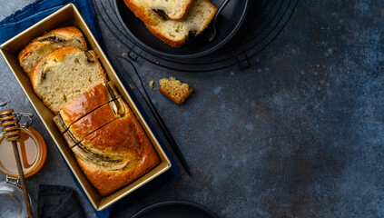 Delicious banana bread or cake in a baking dish on a blue background. Cut pieces of bread in a plate. Fruit cake. Copy space. Top view