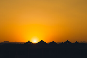 Fototapeta na wymiar Majestic dusk in tropics. Goden sunset sky with beautiful silhouette roofs beach umbrellas and mountains in the evening. Warm orange colors. Abstract nature and travel background. Egypt summer.