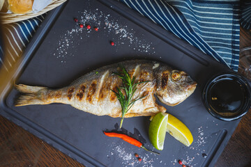 Grilled fish on a plate with a glass of wine and baked vegetables.