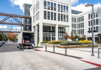 Big rig semi truck with open box trailer unloading goods of the clients moving to a new multilevel...