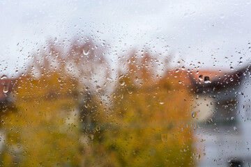 Rain falls on the window on an autumn day. Weather and season concept. Close up, selective focus