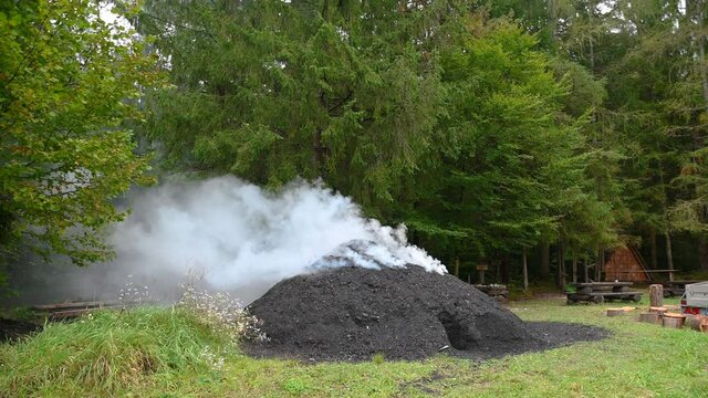 A mound of soil is smoking while charcoal is being made in rural Slovenia. Pile of steaming coal. Traditional production of charcoal from hardwood. Static shot, real time