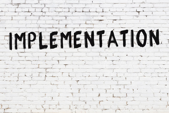 Inscription implementation painted on white brick wall