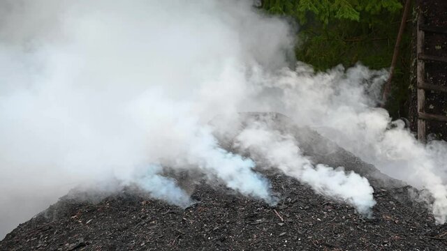 A mound of soil is smoking while charcoal is being made in rural Slovenia. Pile of steaming coal. Traditional production of charcoal from hardwood. Static shot, real time