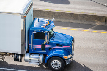 Blue day cab middle class rig semi truck with box trailer driving on the highway road for timely delivery