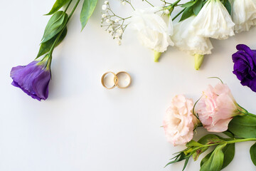 Flowers and two golden wedding rings on white background. Top view.