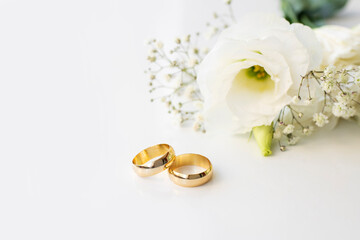 White flowers and two golden wedding rings on white background.
