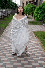 pretty brunette woman in white blanket on the street. crazy beautiful millennial carefree girl