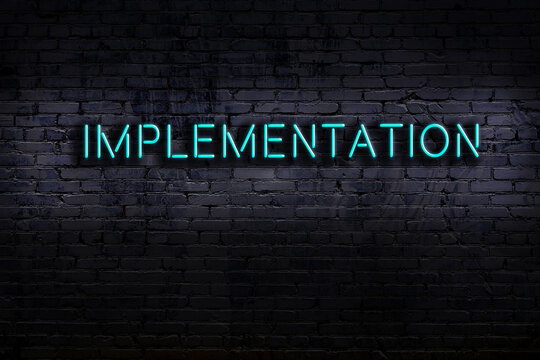 Neon sign. Word implementation against brick wall. Night view