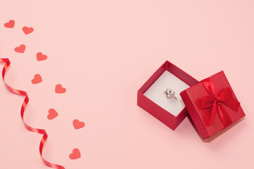 red box with a white gold ring with a precious stone on a pink background with confetti of hearts...