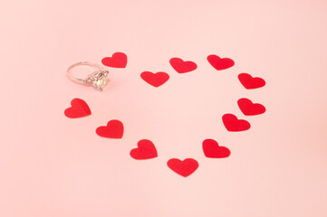 white gold ring with a precious stone on a pink background with confetti in the form of hearts