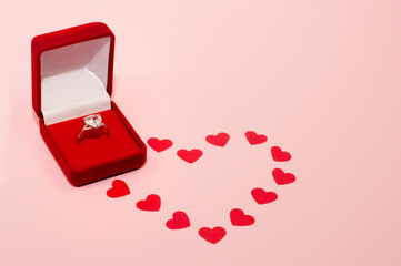 white gold ring with a precious stone in a red box on a pink background with confetti in the form of a heart