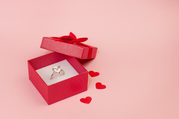 white gold ring with a precious stone in a red velvet box on a pink background with confetti in the...