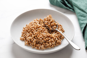 boiled buckwheat porridge with a spoon on a marble table with green napkin