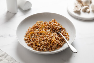 boiled buckwheat porridge with mushrooms with a spoon on a marble table