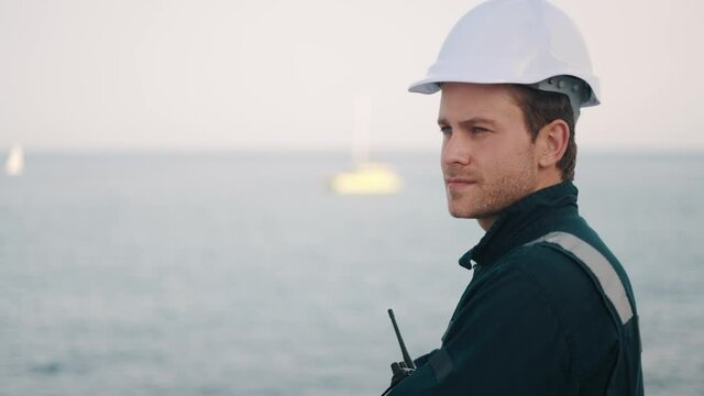 Young handsome man port worker with walkie-talkie in hand controlling work process in shipping port