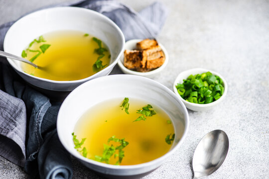 Two bowls of healthy chicken broth with croutons, parsley and spring onions