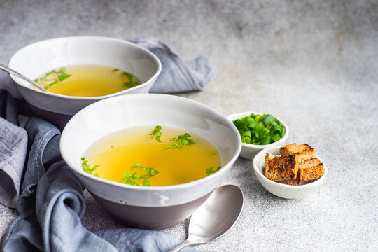 Two bowls of healthy chicken broth with croutons, parsley and spring onions