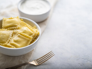 Dinner table for one person. On a white tablecloth, a serving of classic Italian ravioli, sour cream sauce and a fork. There are no people in the photo. Restaurant, cafe, hotel, home cooking.
