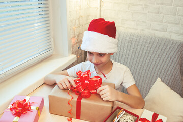 A child in a Santa Claus hat looks in surprise at a huge Christmas gift box with a big red bow. 