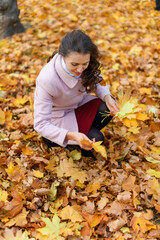 Portrait of a woman in an autumn park. She is gathering yellow maple leaves in a glade.