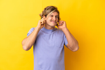 Handsome blonde man isolated on yellow background frustrated and covering ears