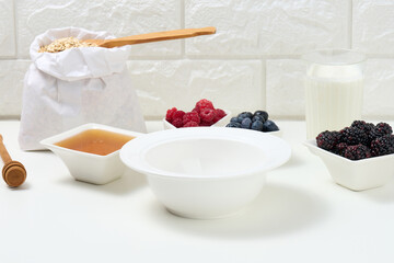 empty white round ceramic plate, oatmeal and fruit for cooking porridge on a white table