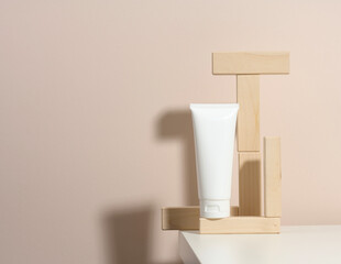 empty white plastic tubes for cosmetics on a beige background with wooden blocks. Packaging for cream, gel, serum, advertising and product promotion, mock up