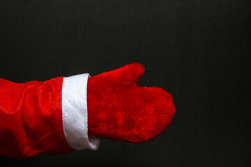 Mock up hand of santa claus in red mittens on a black background. Close-up. New Year concept. copy space