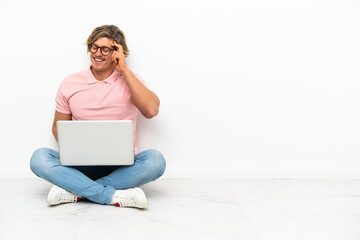 Young caucasian man sitting on the floor with his laptop isolated on white background laughing