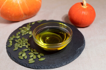 close-up of natural pumpkin seed oil in a bowl and pumpkin seeds on a black board, soft focus.